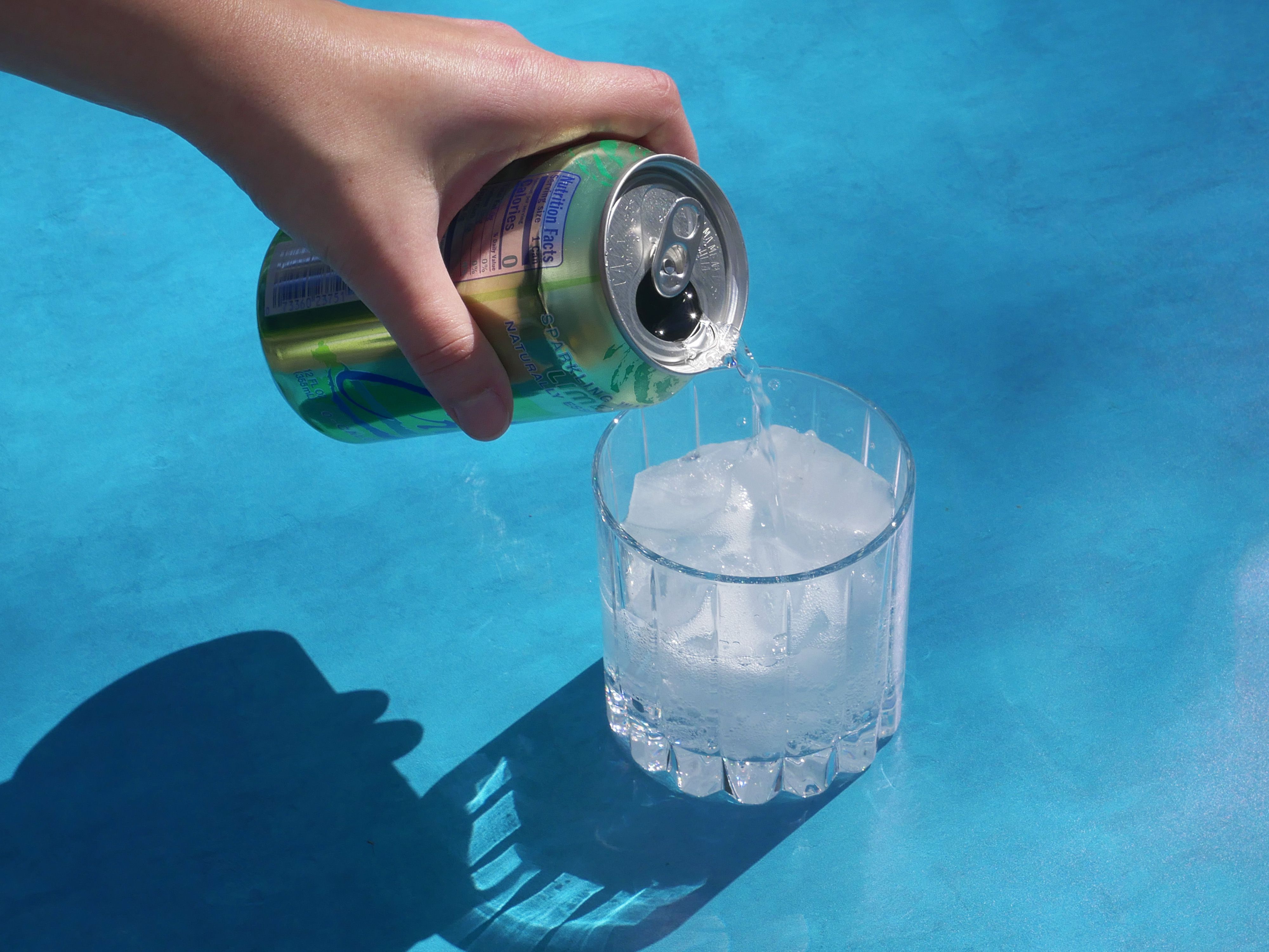 pouring seltzer into the riedel glass on a blue surface