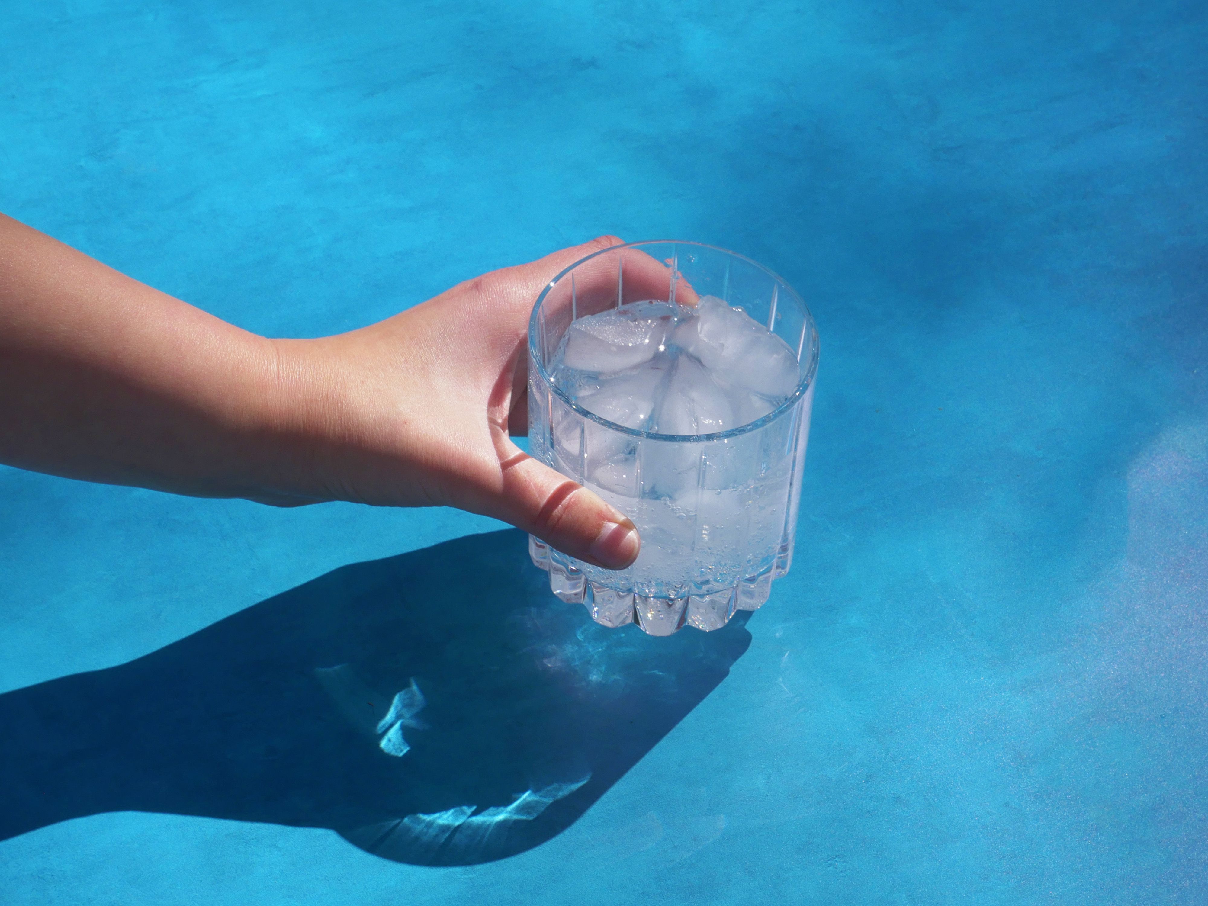 hand holding seltzer with ice in riedel over blue surface