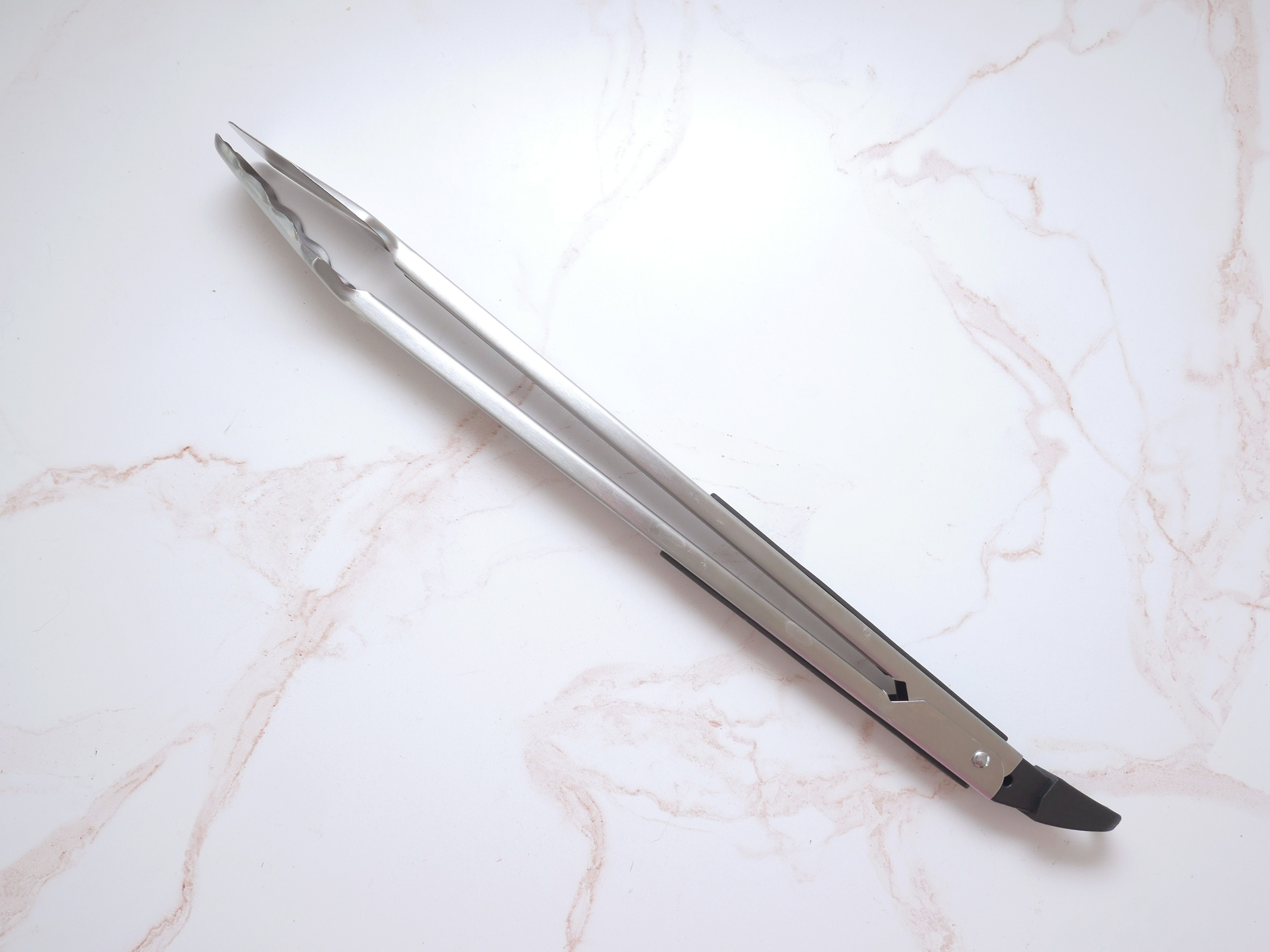 broil king grill tongs on a pink and white marble surface
