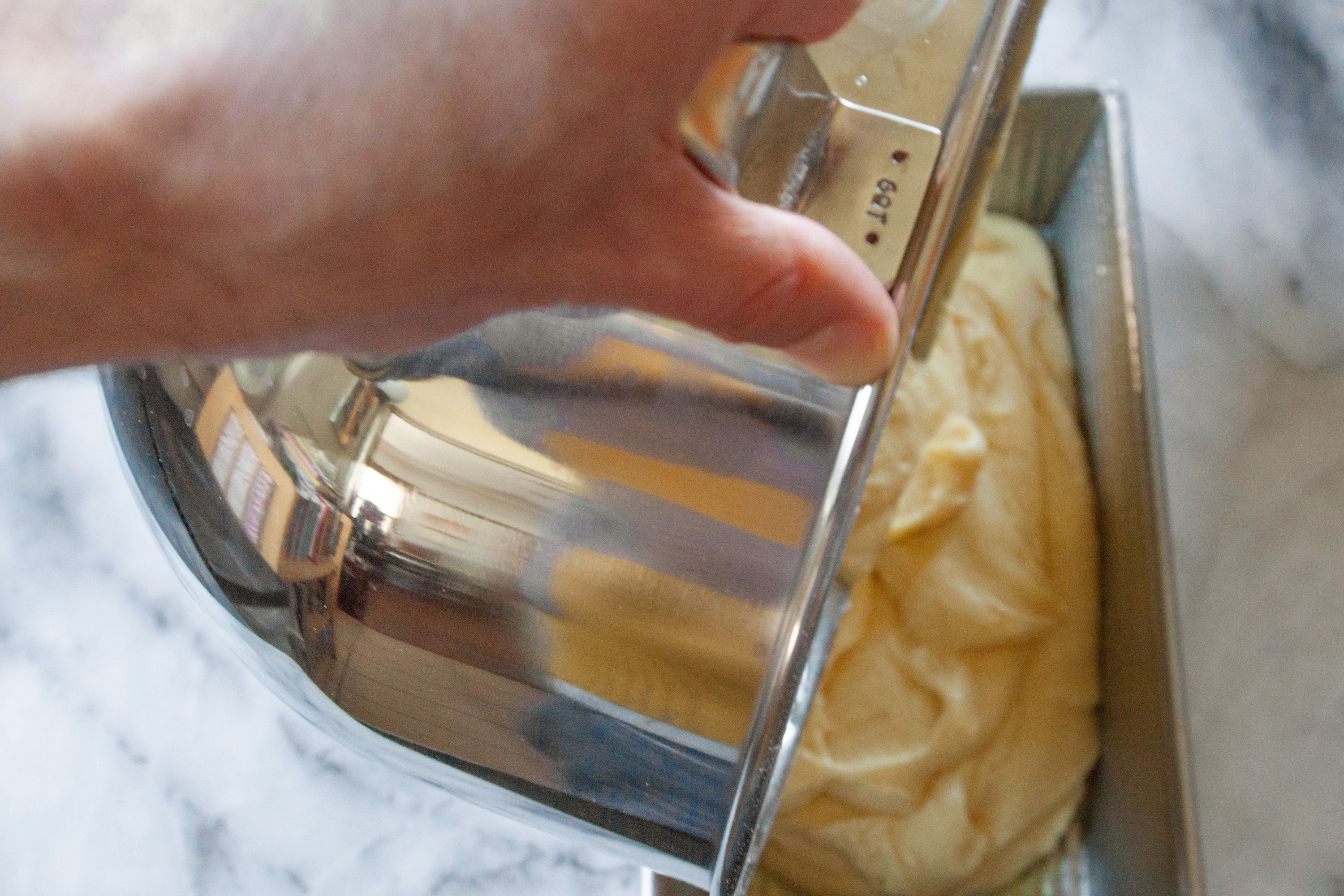 A person pouring batter from a stand mixer bowl into a loaf pan