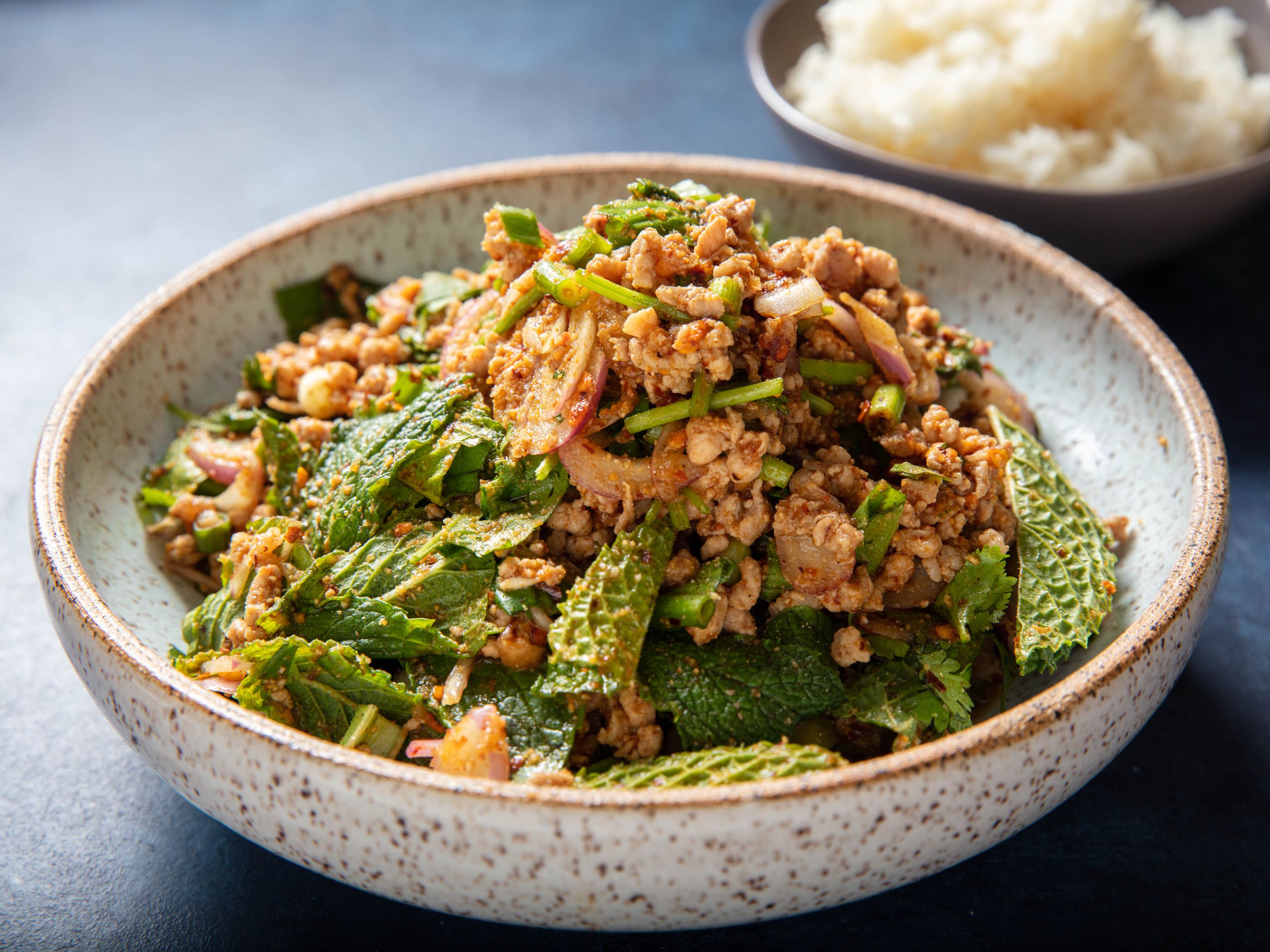 Serving bowl of pork laab with a bowl of sticky rice in the background