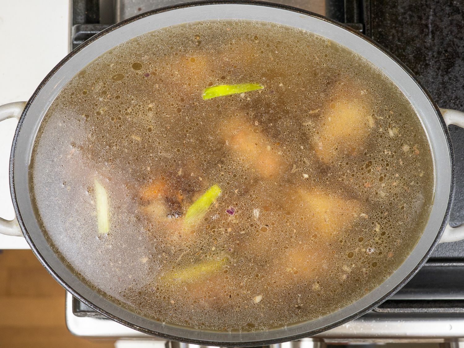 Oxtails and aromatics covered in water in a Dutch oven