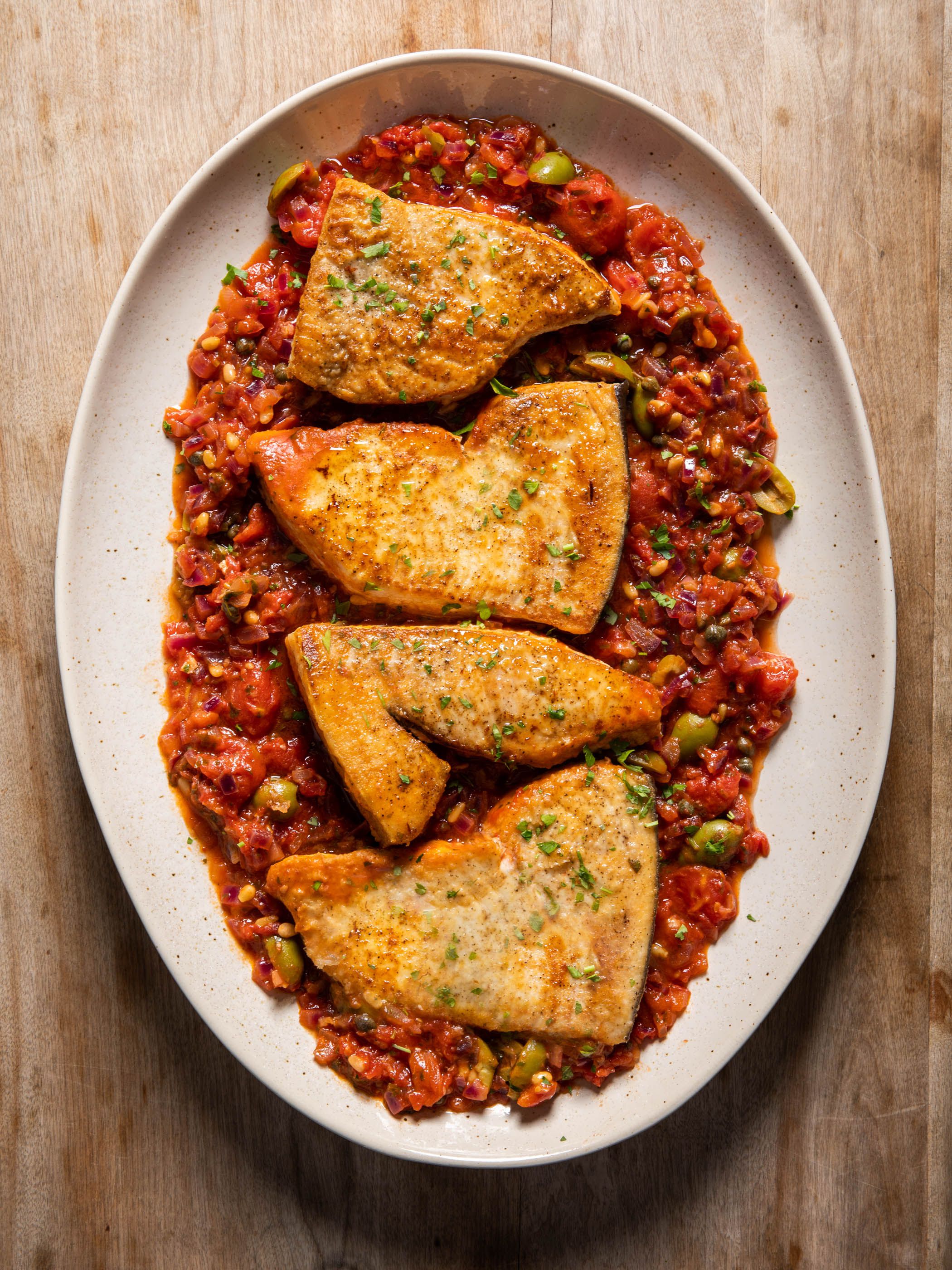 Braised swordfish steaks piled into an ovular white dish.