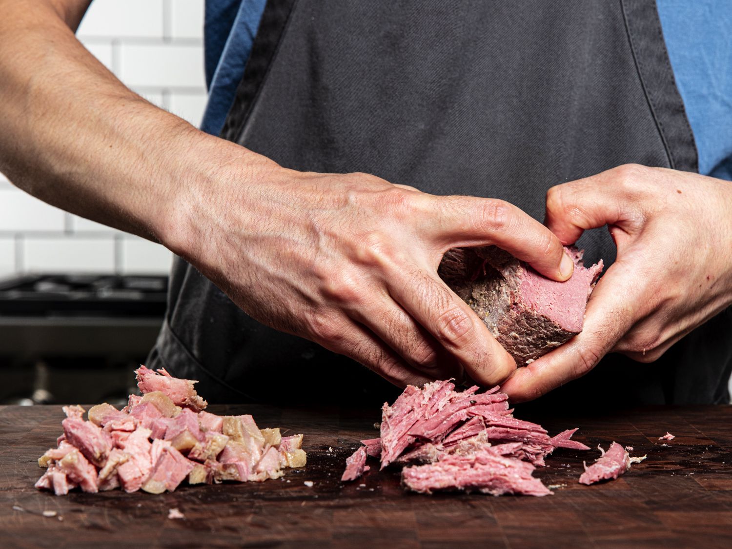 Hands ripping corned beef into piles on a cutting board