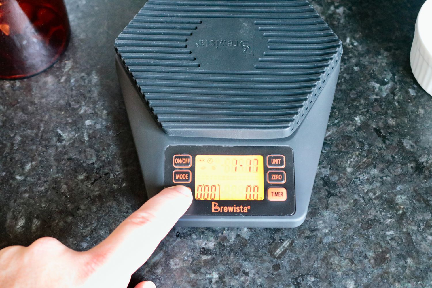 the brewista on a countertop with a finger reaching out and touching the mode button