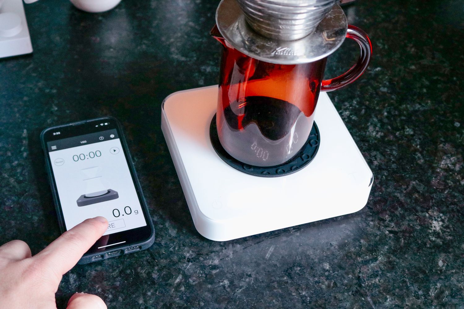A hand tapping the app of the Acacia Pearl S, which is beside the phone