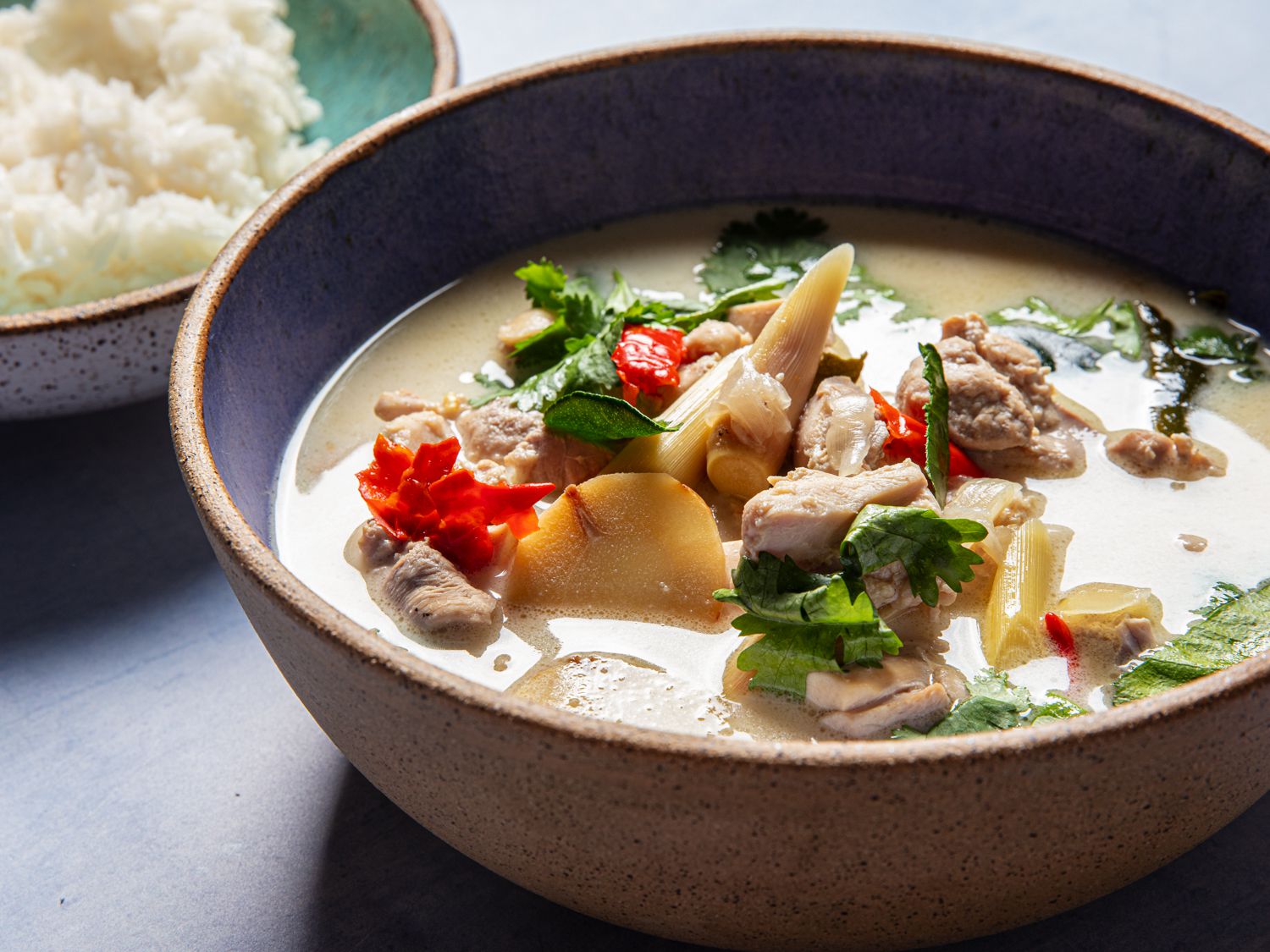 Side view of finished tom kha gai next to a bowl of rice