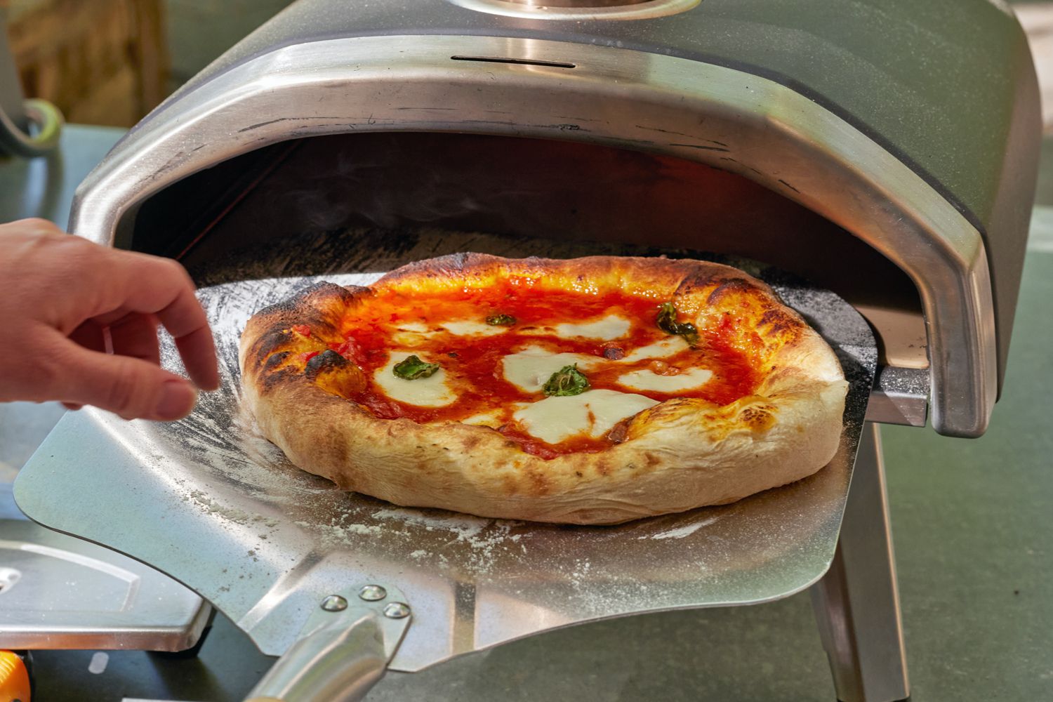 A pizza being turned with a metal pizza peel in the Ooni Fyra 12