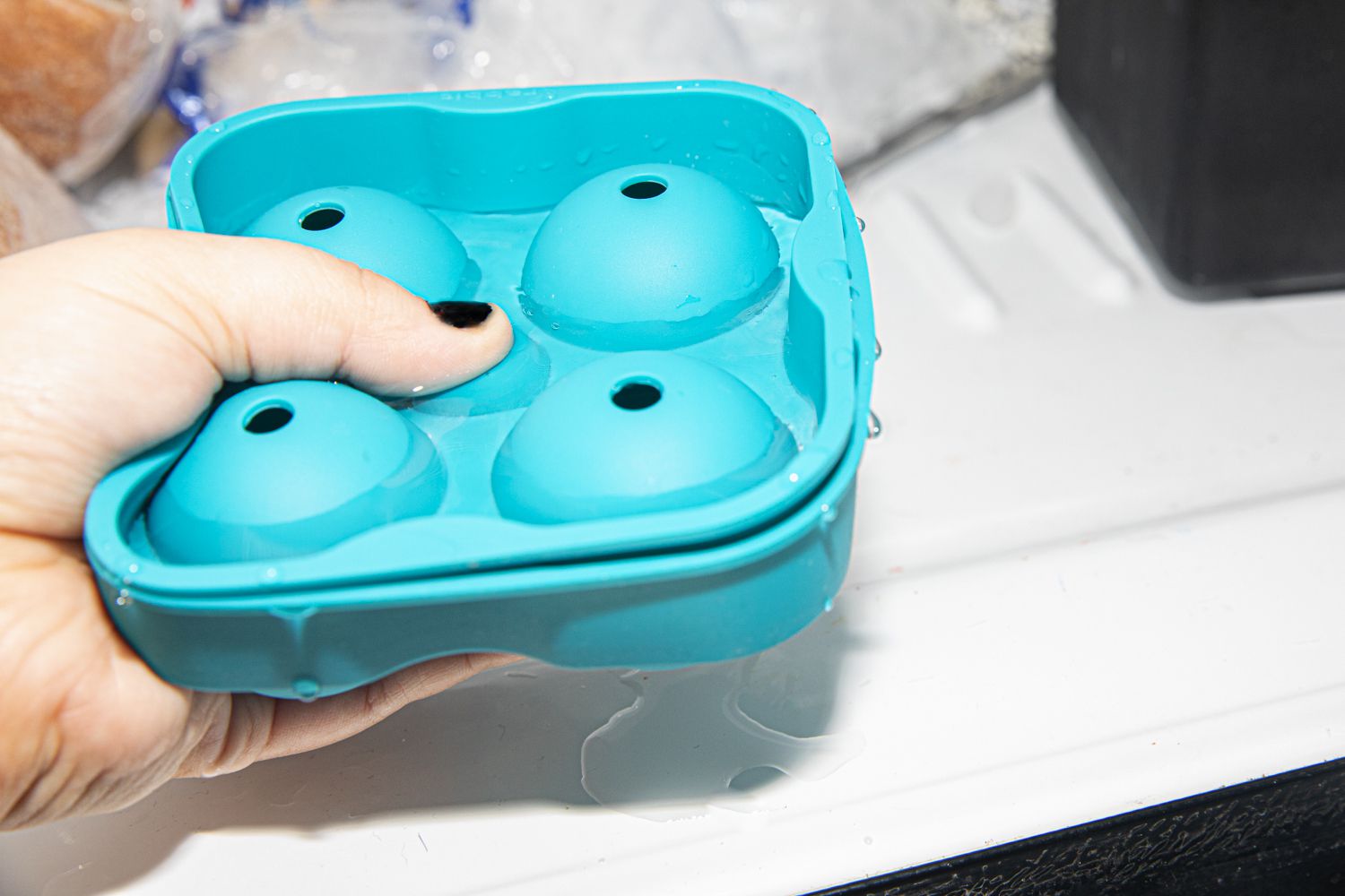 A hand holding a silicone sphere ice tray and it overflowing