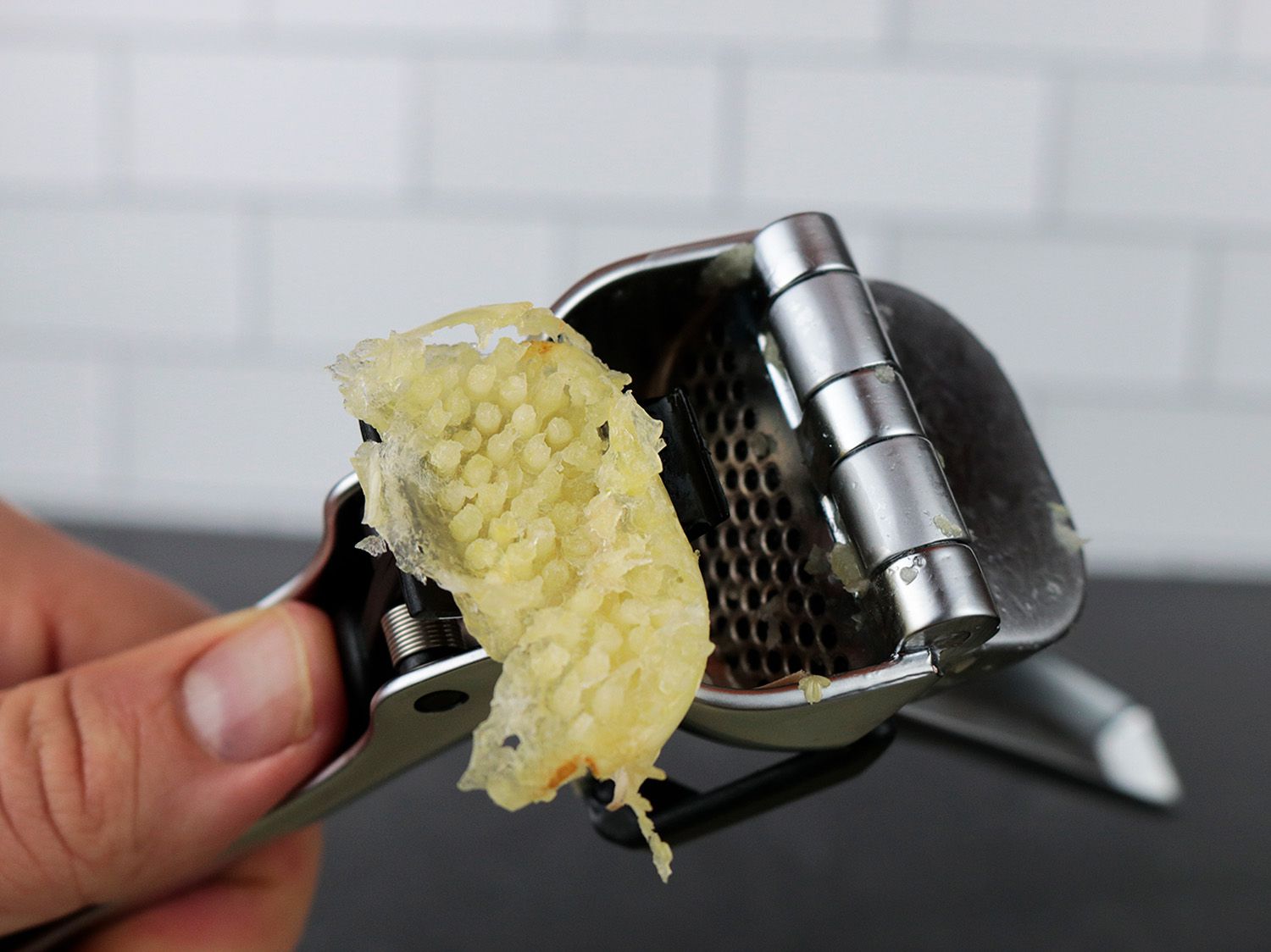 a mashed garlic clove popping out of a garlic press