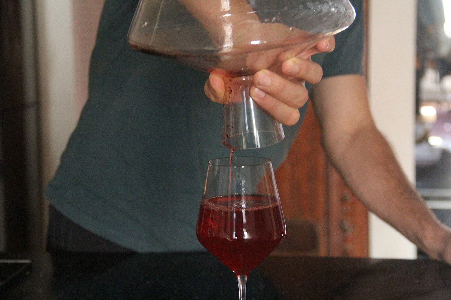 A person holding a decanter vertically over a wine glass as wine drips out of the decanter