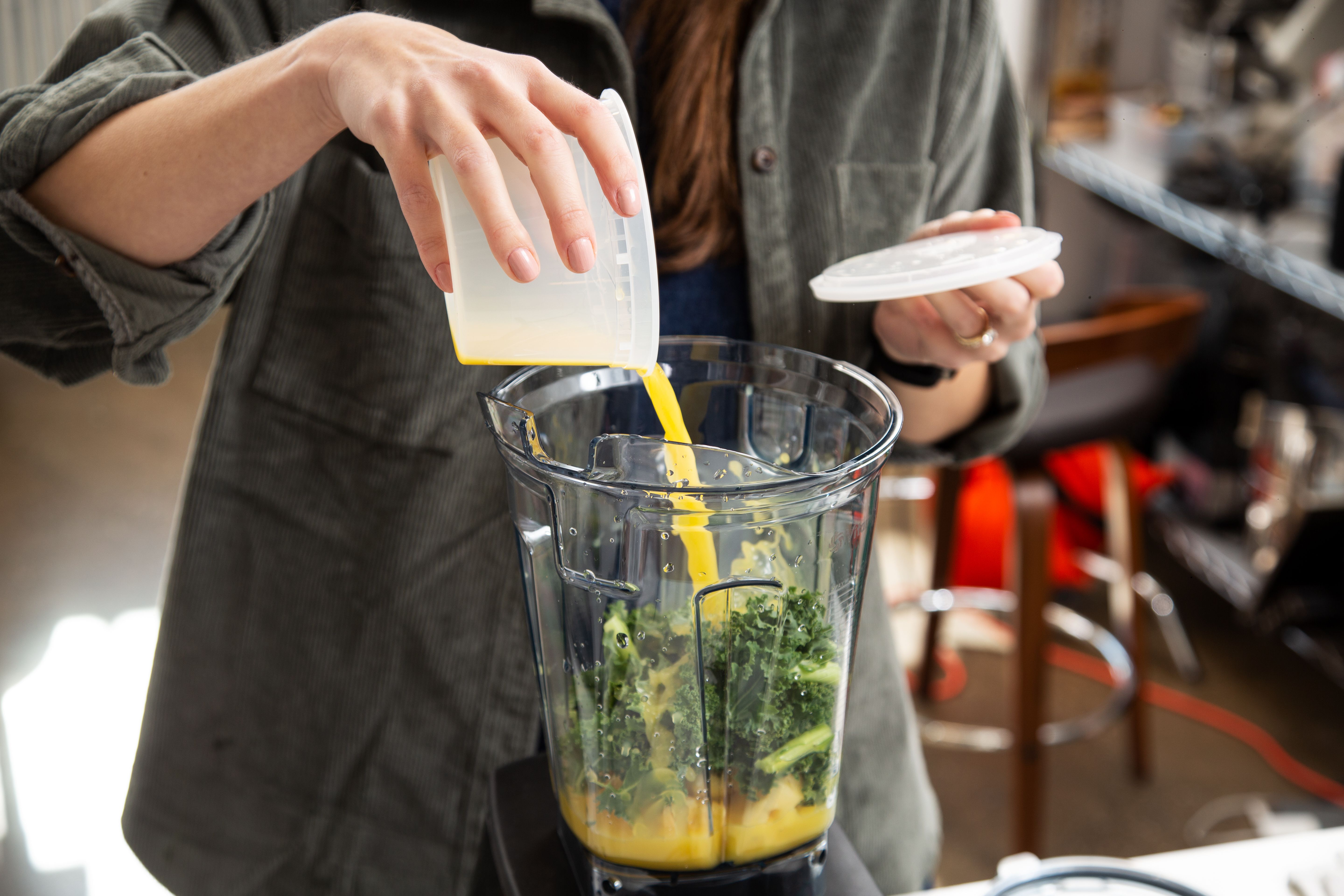 someone adding orange juice to a full-sized blender