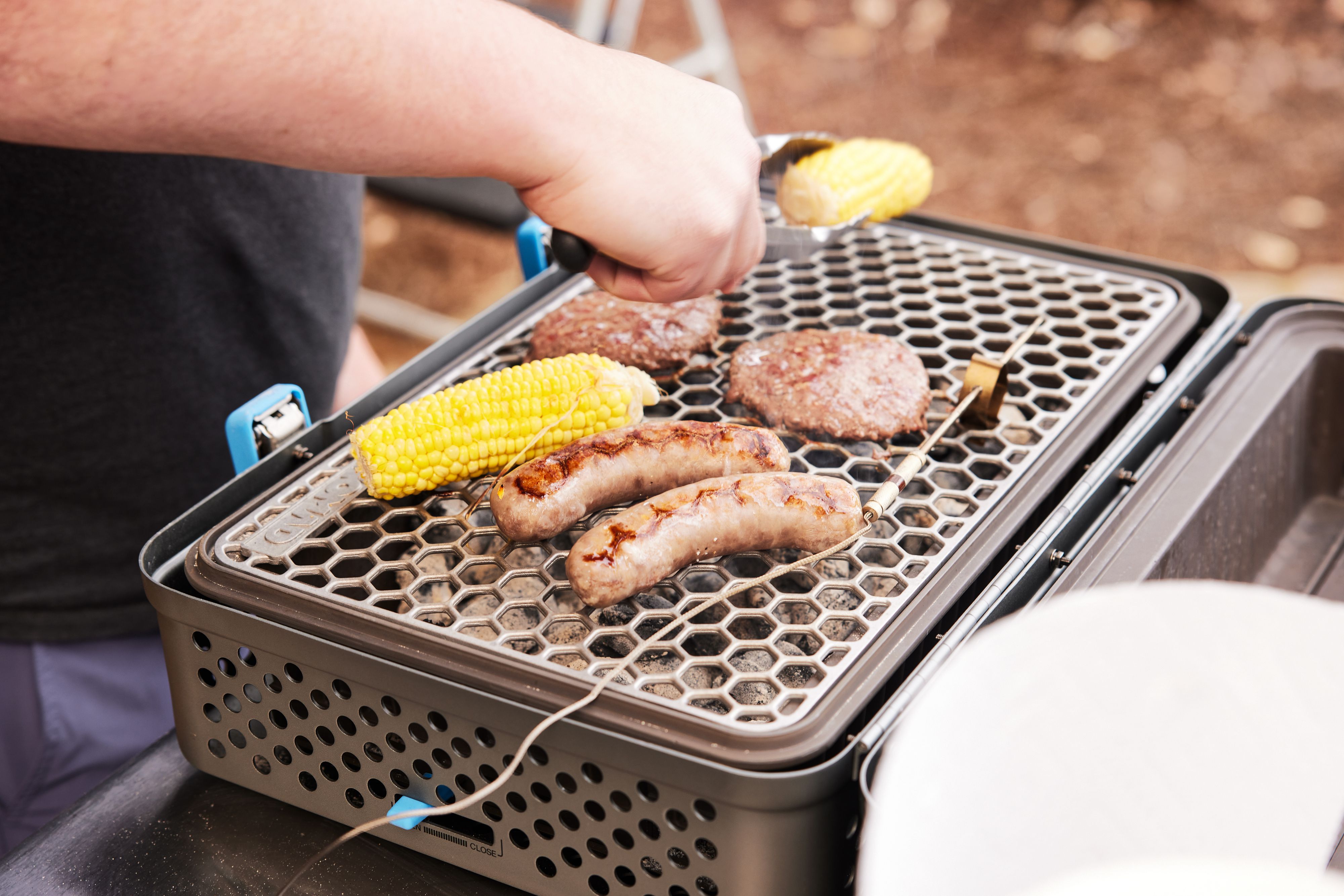 a person flipping corn on a portable charcoal grill