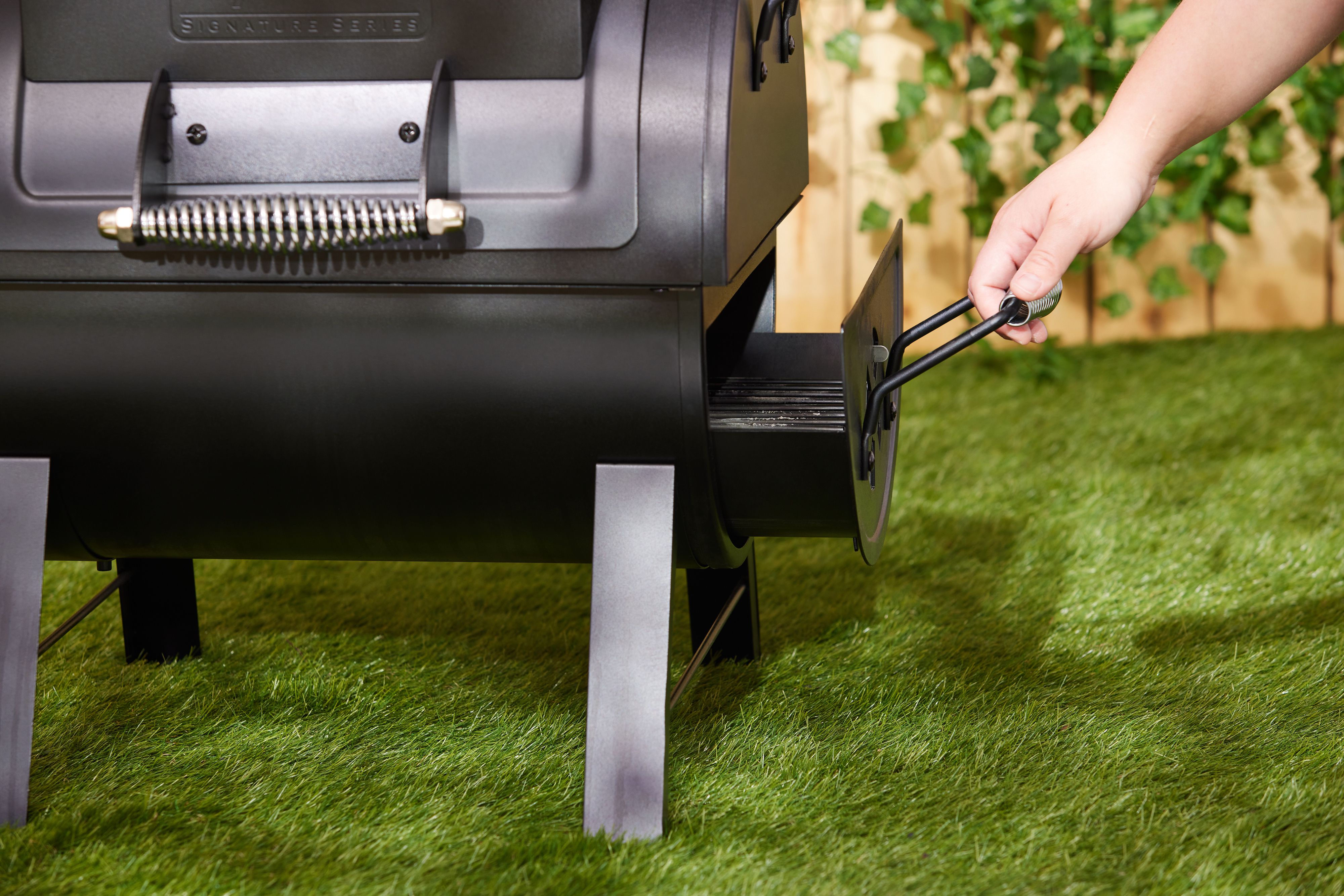 A hand pulling out a portable charcoal grill's ash catcher