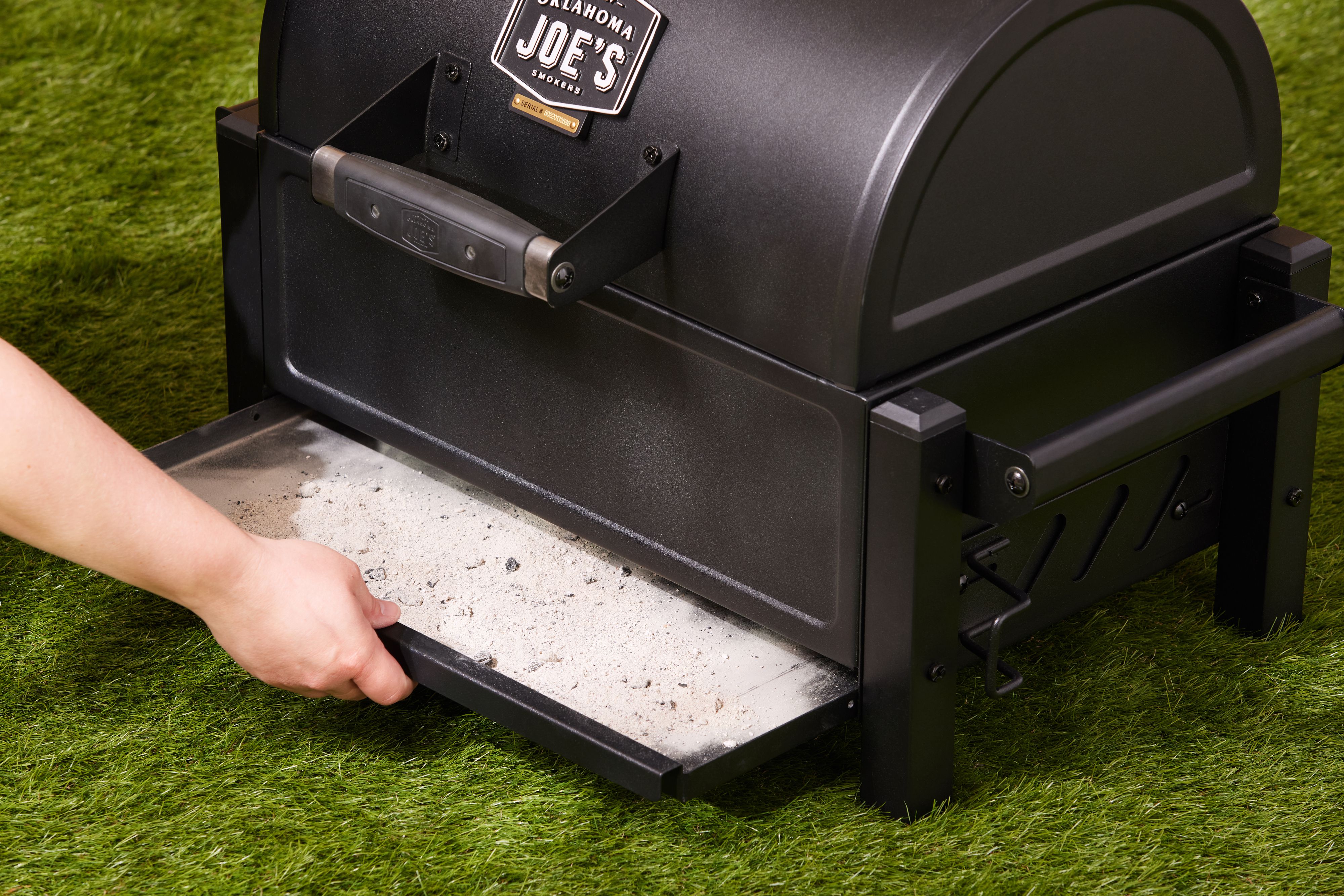 A hand pulling out the ash tray of a portable charcoal grill