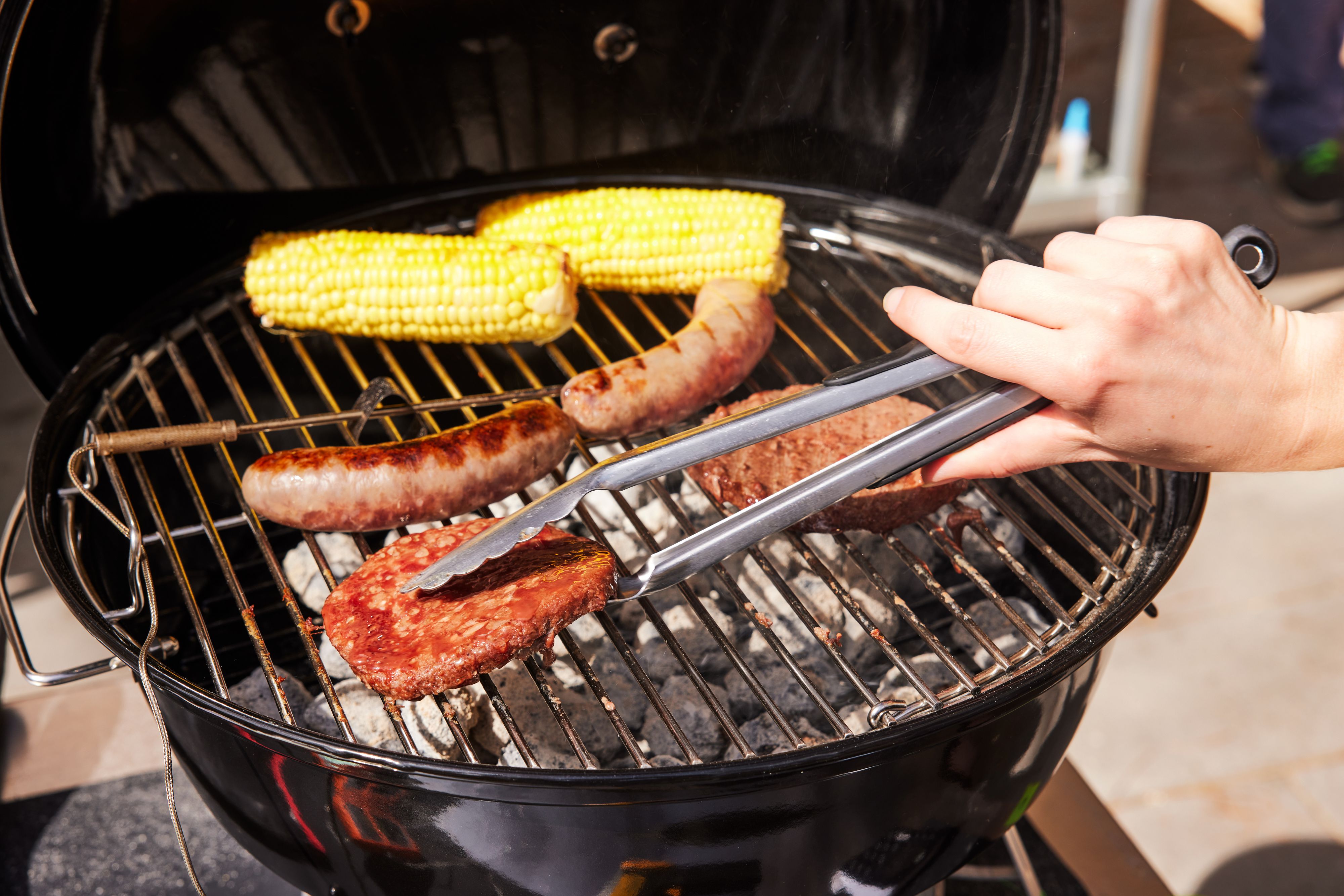 tongs flipping a burger on a portable charcoal grill
