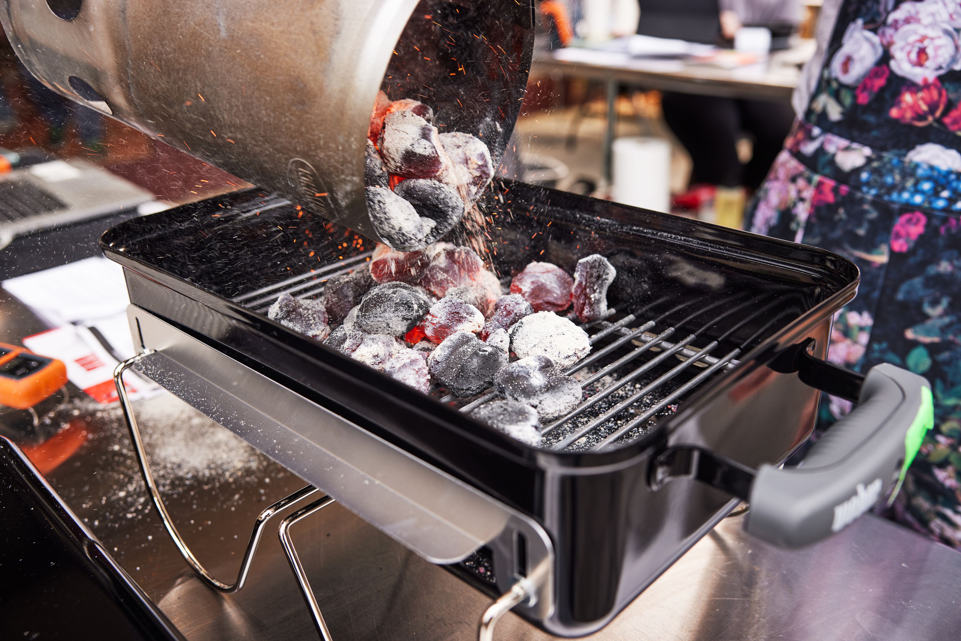 A person adding hot charcoal to a portable charcoal grill