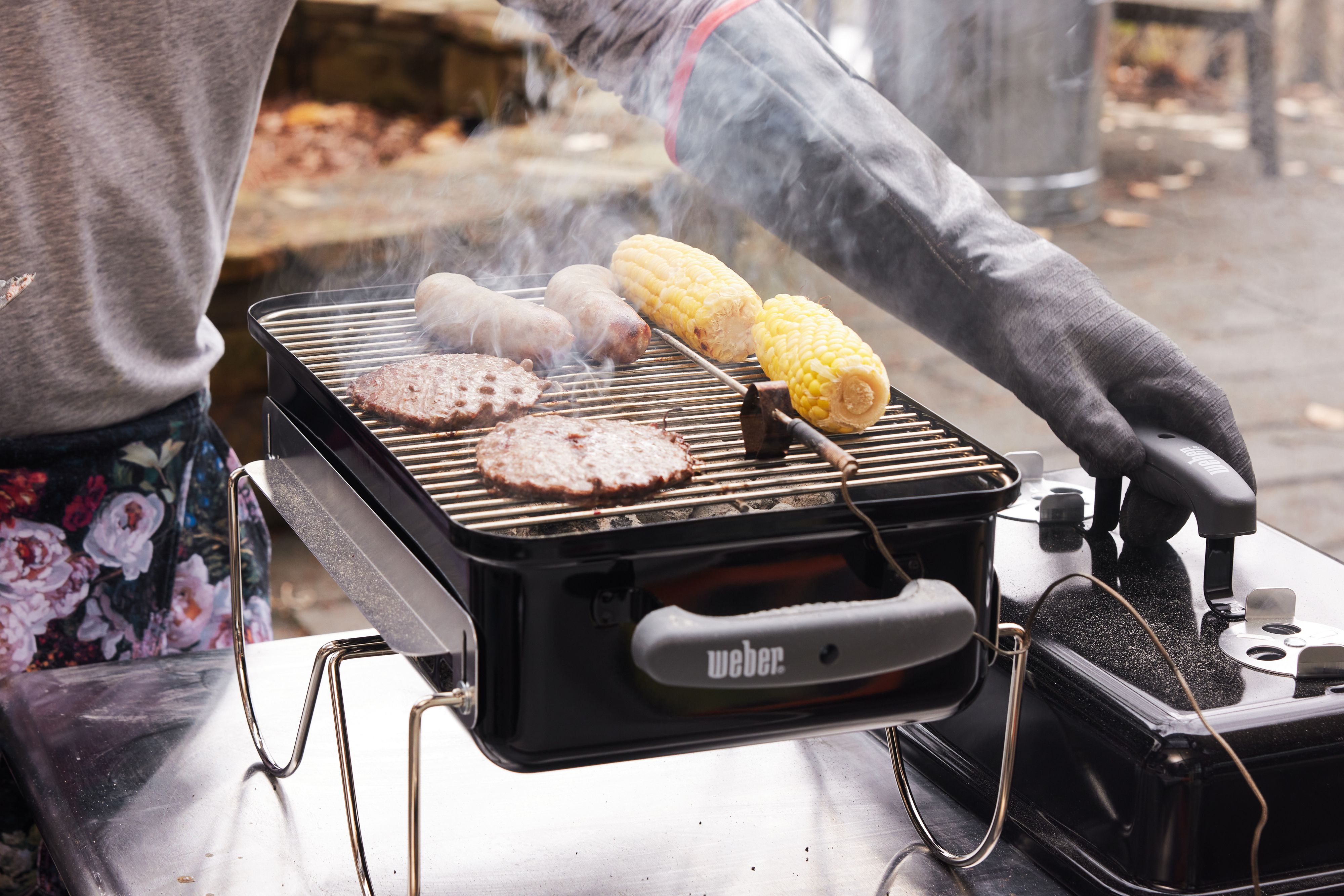 burgers, brats, and corn cooking on a portable charcoal grill