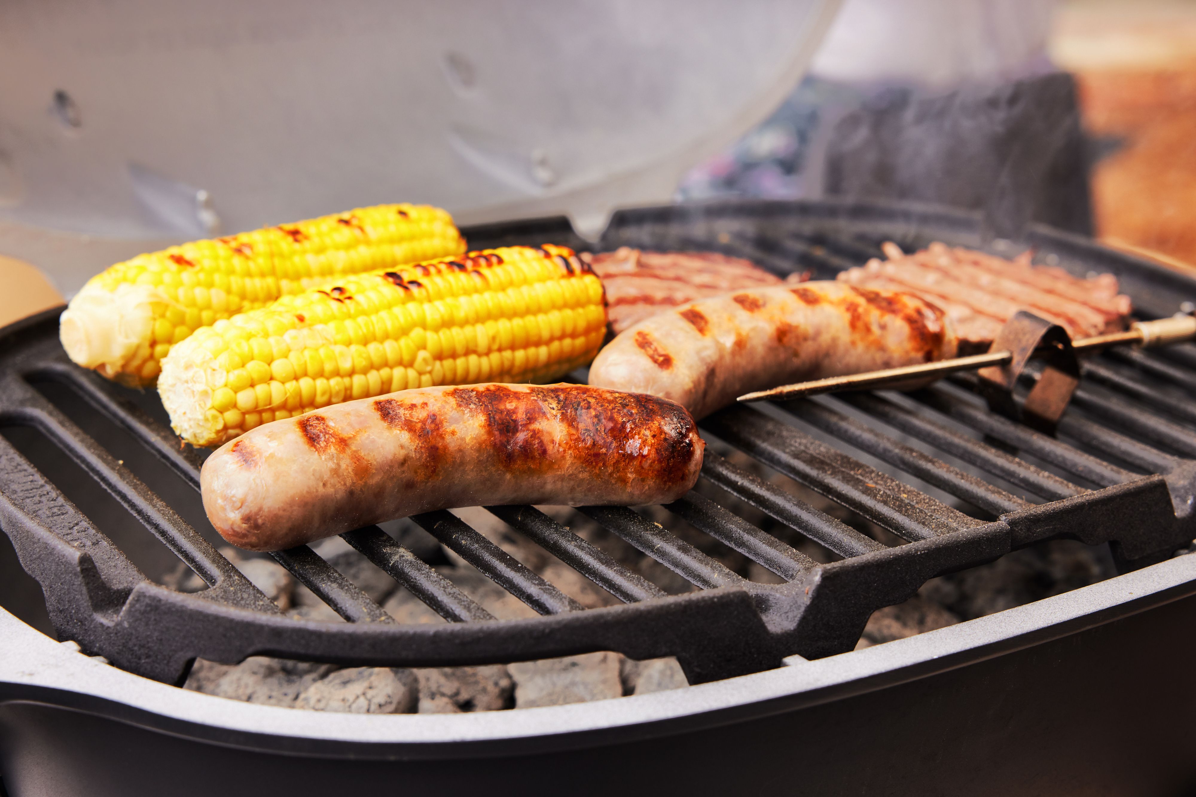 a closeup look at sausages and corn grilling on a portable charcoal grill