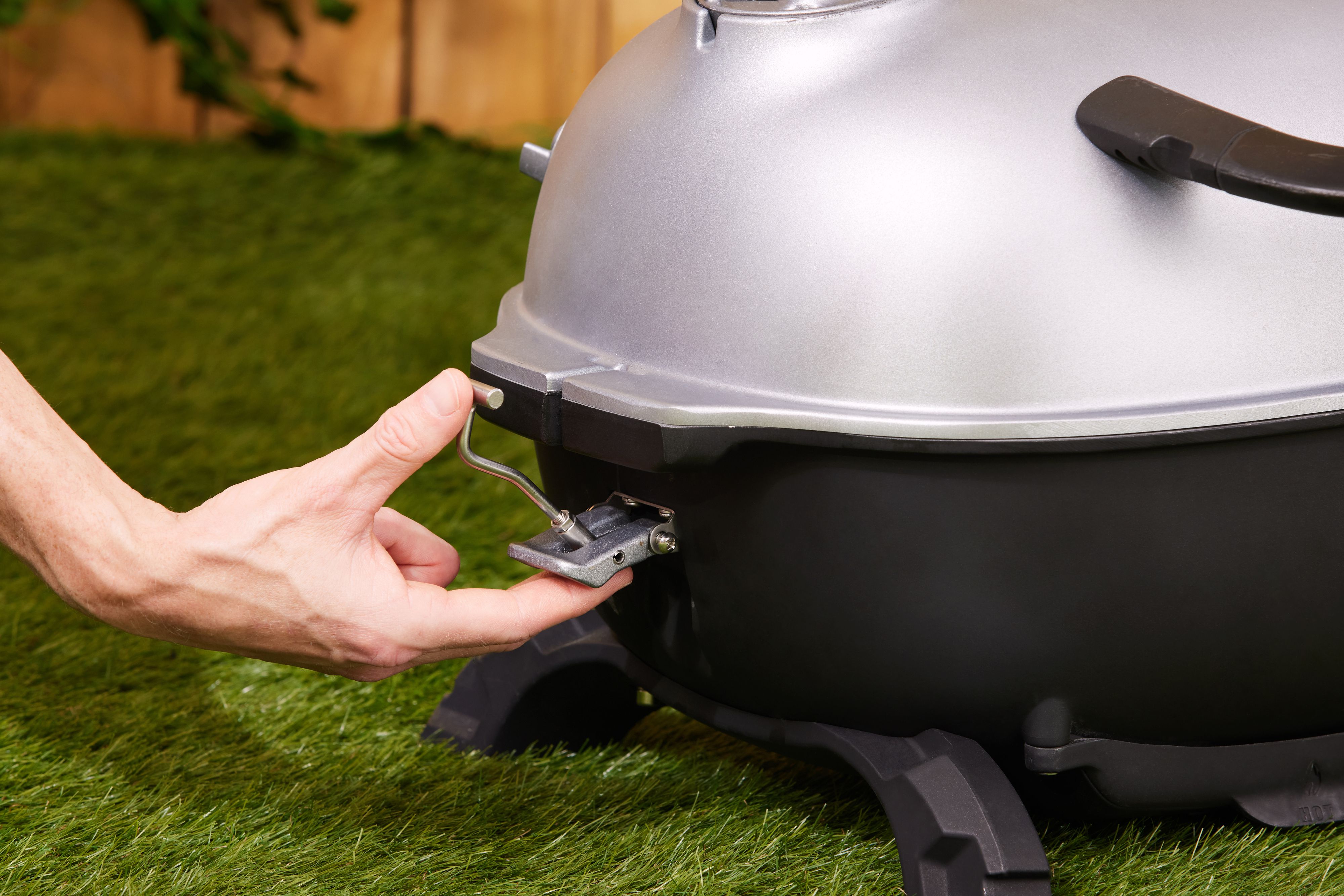 A hand closing the clip on a portable charcoal grill's lid