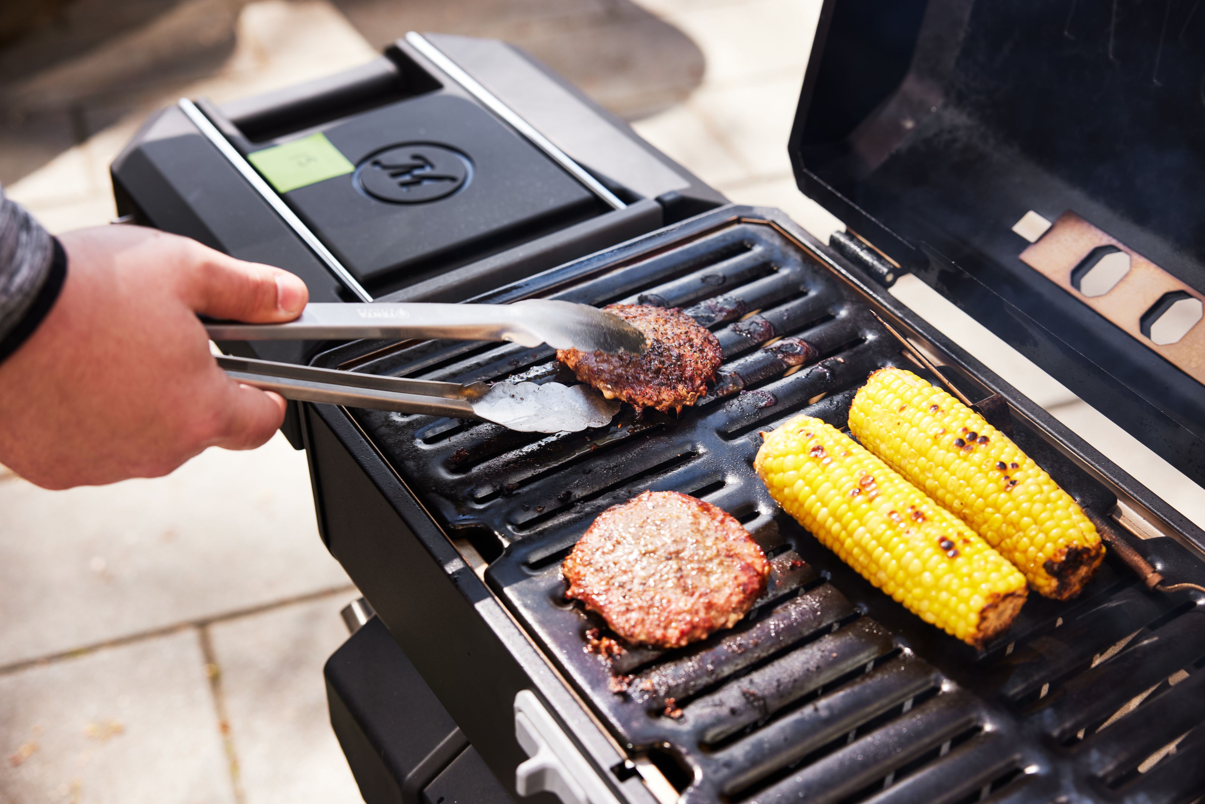 Tongs flipping a burger on a portable charcoal grill