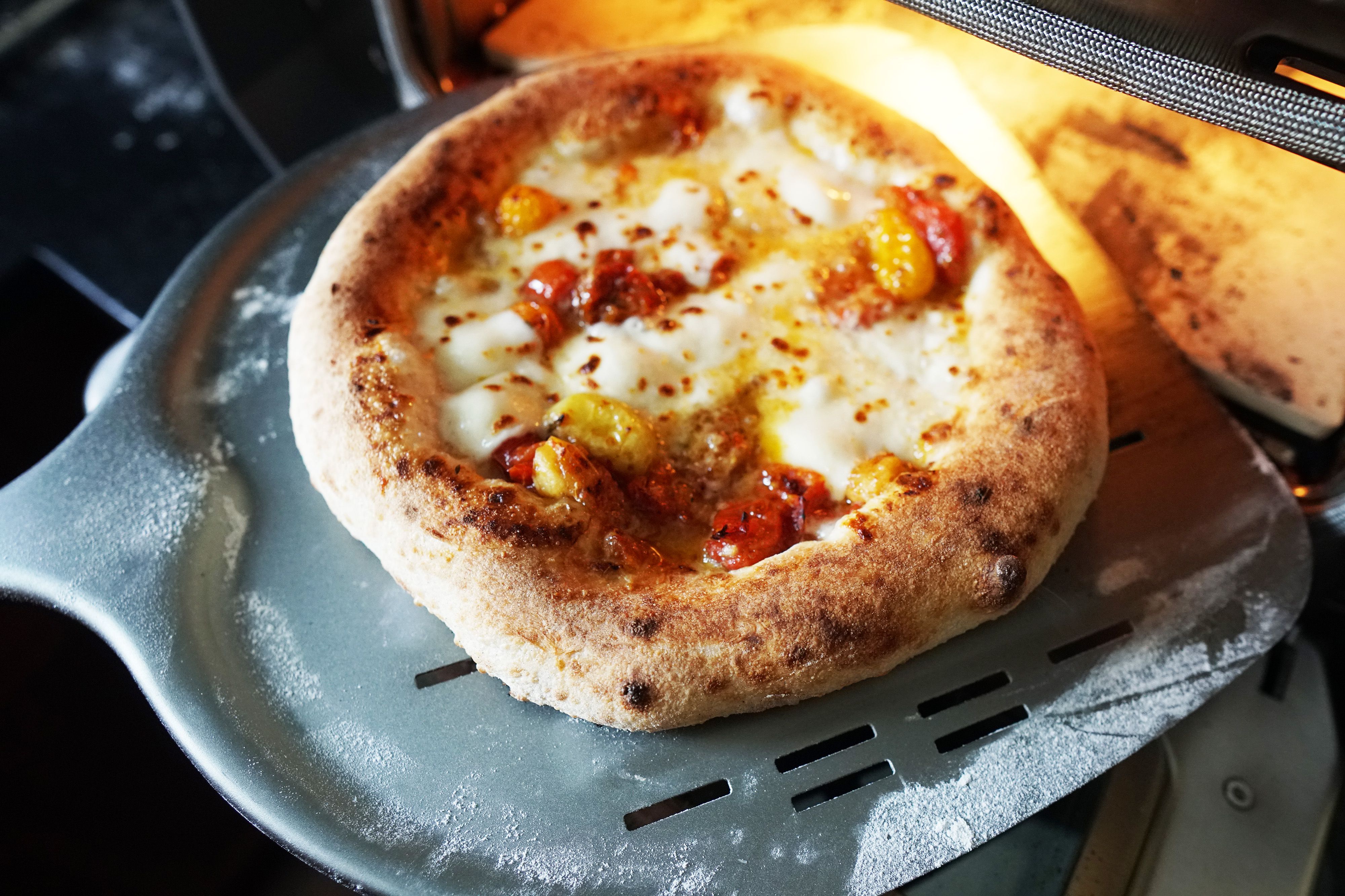 A closeup of a pizza coming out of the Ooni Volt on a pizza peel