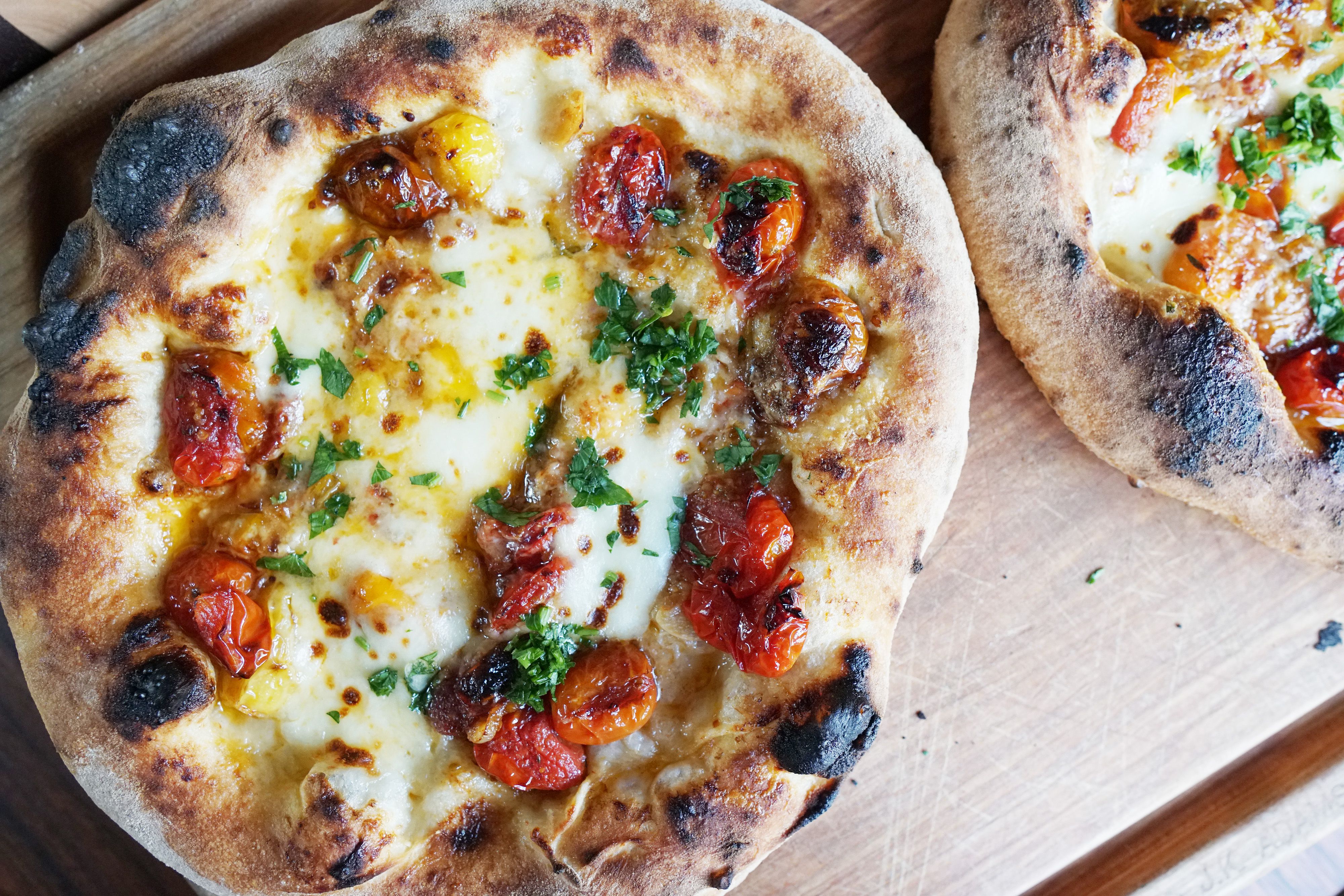 A closeup look at two pizzas on a wooden cutting board